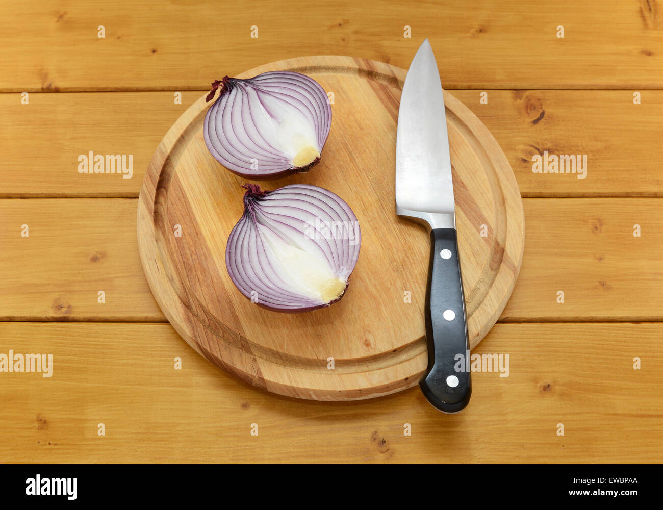 La cebolla roja cortada en la mitad con un cuchillo de cocina afilado sobre una tabla de cortar sobre una tabla de madera Foto de stock