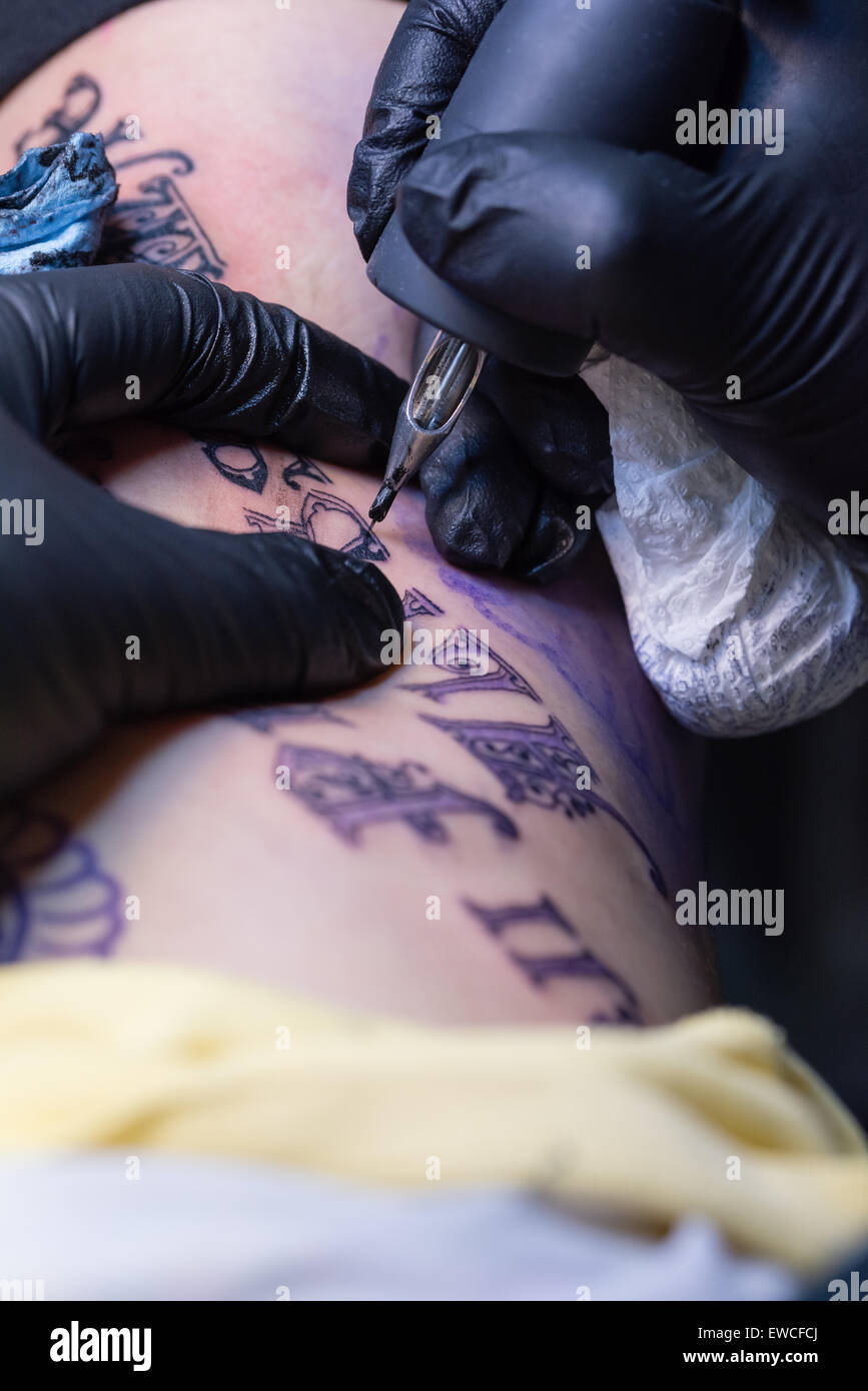 Una mujer obteniendo un script negro tatuaje en la caja torácica. Foto de stock