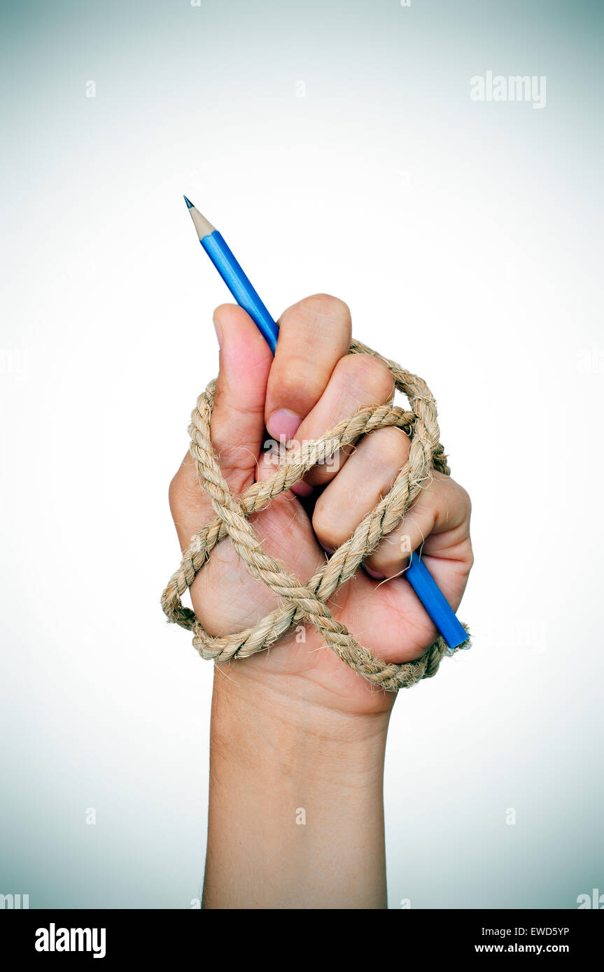 La mano de un hombre atado con una cuerda, sosteniendo un lápiz, representando la idea de la represión de la libertad de prensa o la libertad de expressio Foto de stock