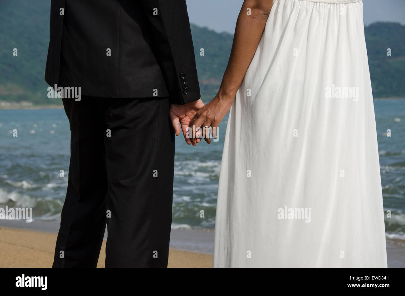 Pareja de amantes de la fotografía de bodas en la playa caminando tomados de las manos abrazando riendo Interracial par Foto de stock