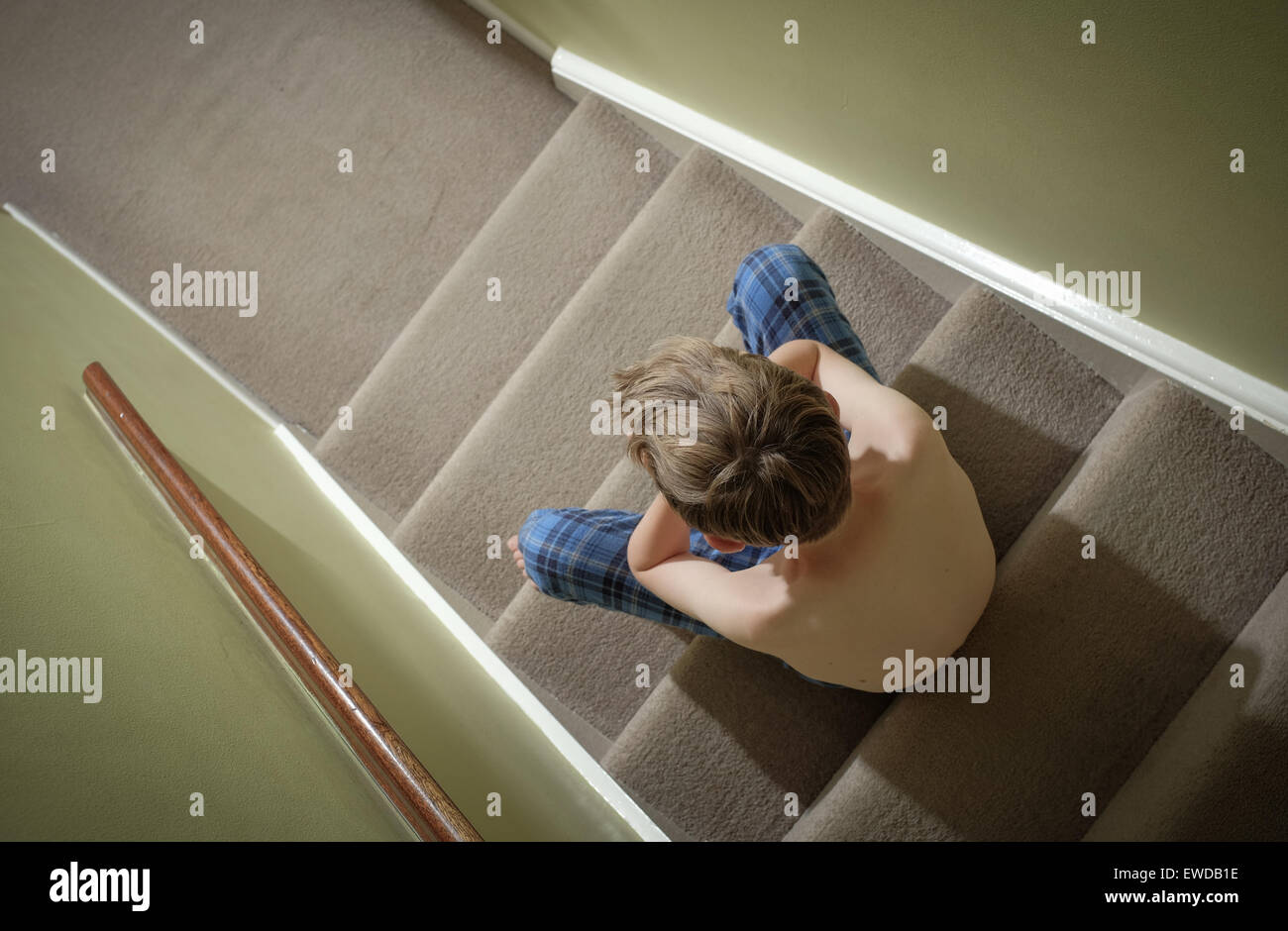Un niño sentado en las escaleras con su cabeza en sus manos mirando disgustado Foto de stock