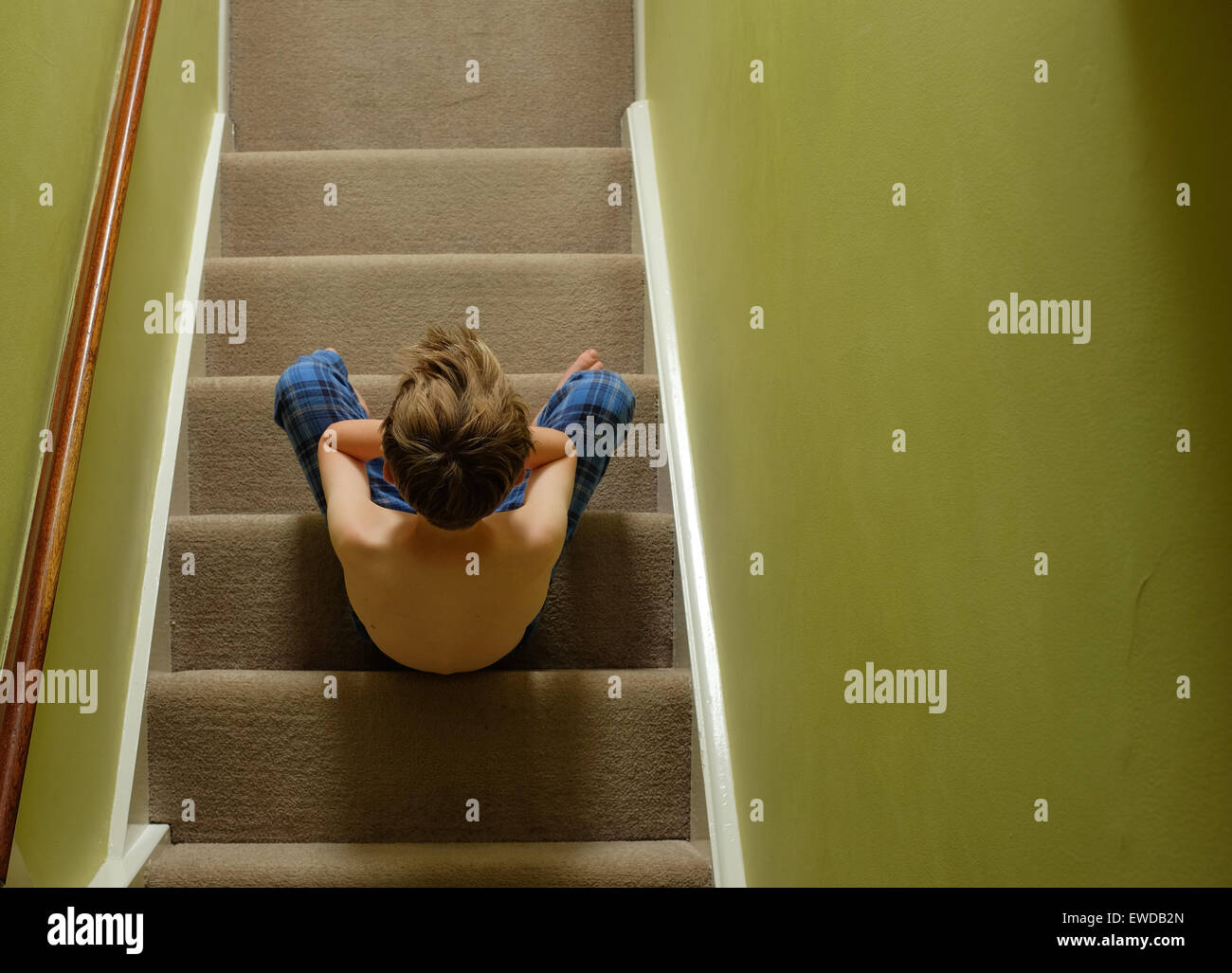 Un niño sentado en las escaleras con su cabeza en sus manos mirando disgustado Foto de stock
