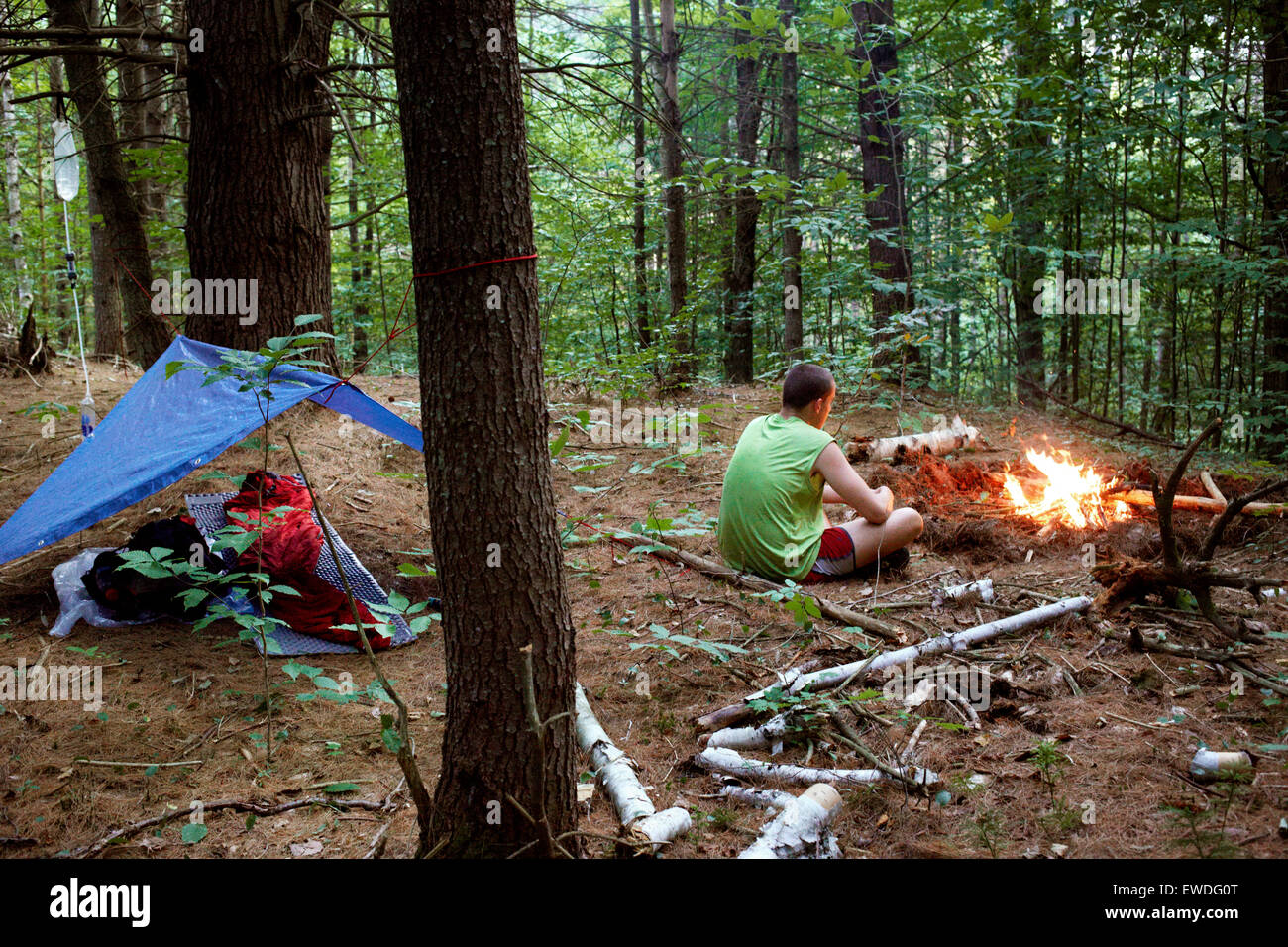 Un excursionista tiende a un pequeño fuego de campamento junto a su vivienda. Foto de stock