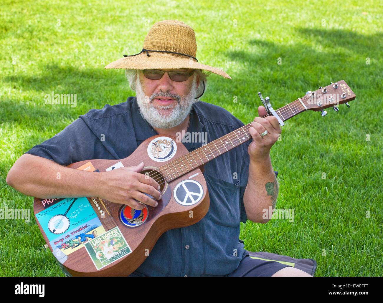 Un hombre se sienta sobre un césped y toca la guitarra en un día de verano en Farewell Bend Park, Bend, Oregon Foto de stock