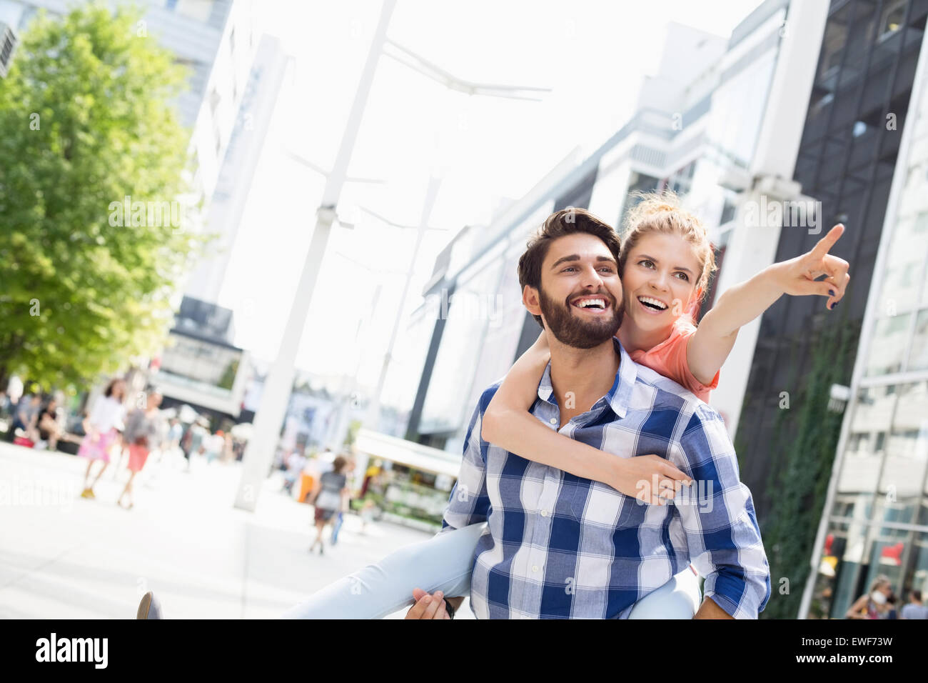 Mujer feliz mostrando algo al hombre mientras disfruta piggyback paseo en ciudad Foto de stock