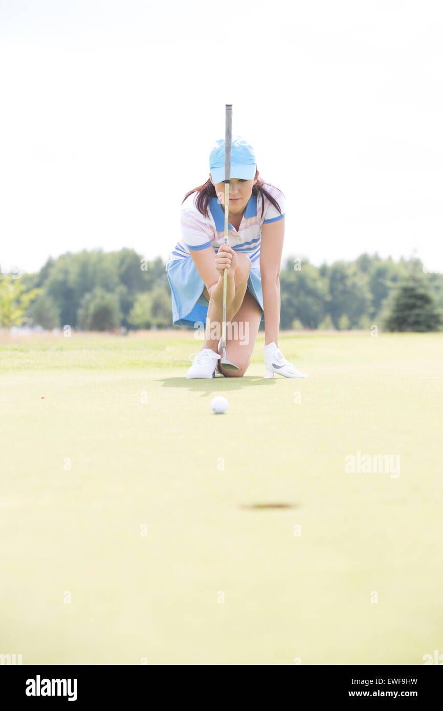 Mujer joven apuntando la bola mientras arrodillado al campo de golf Foto de stock
