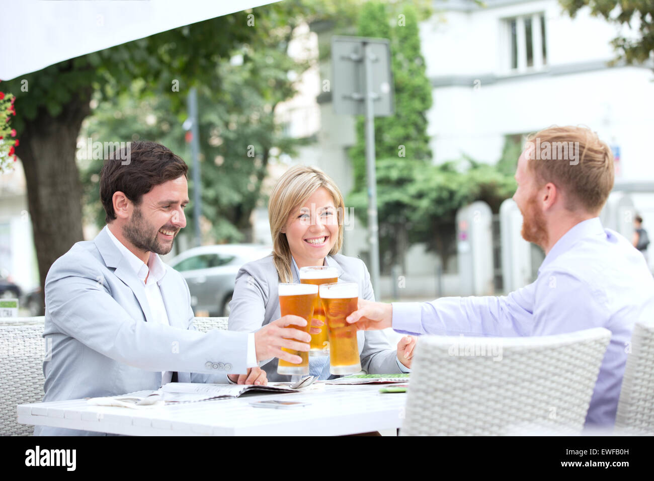 Felices empresarios tostar los vasos de cerveza en el restaurante al aire libre Foto de stock