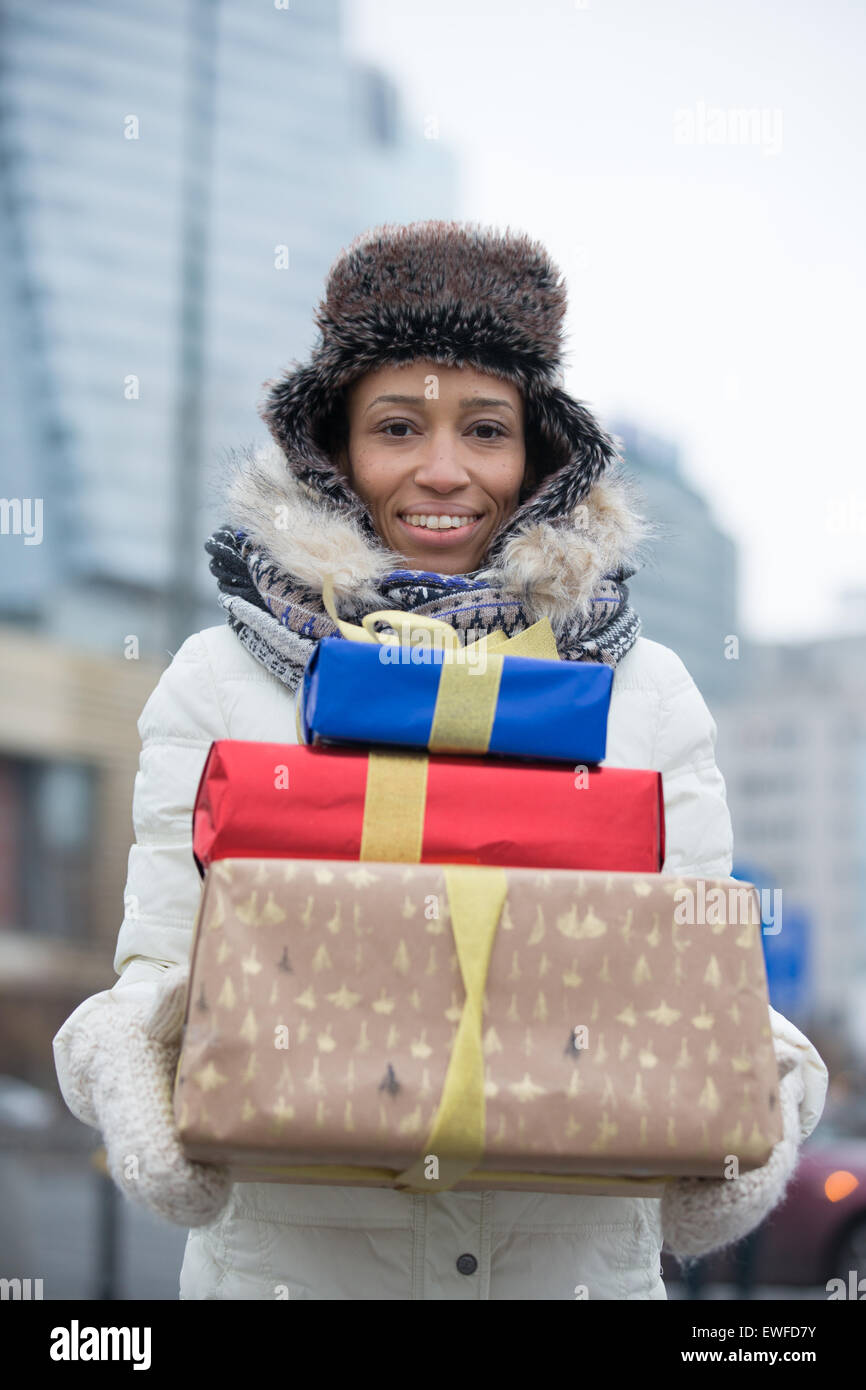 Retrato de mujer alegre y llevar regalos apilados durante el invierno Foto de stock