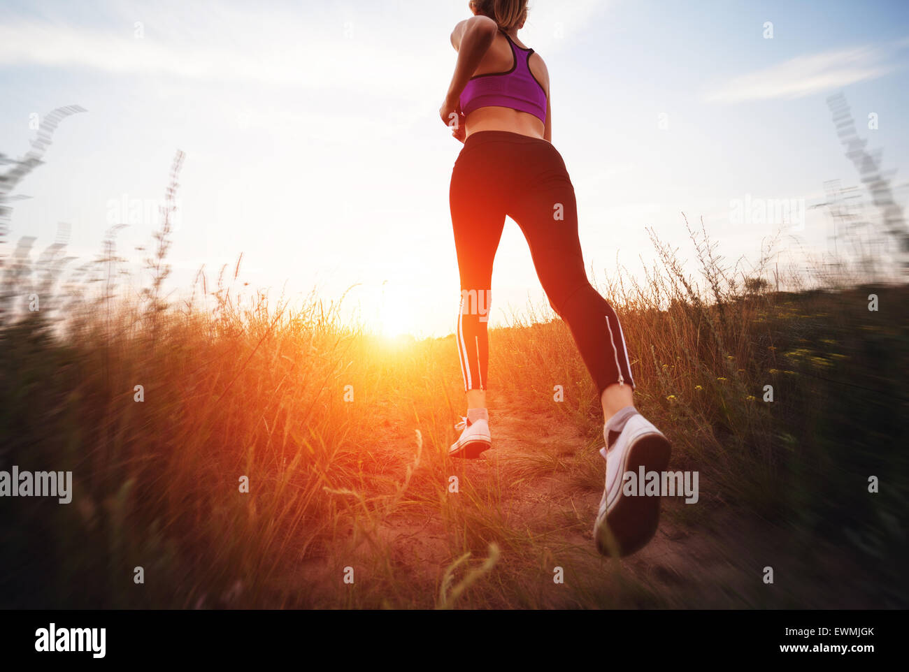 Mujer joven corriendo en un camino rural al atardecer en el verano del campo. Antecedentes deportivos en el estilo de vida Foto de stock