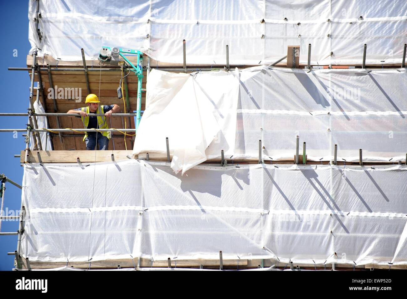 Un trabajador de la construcción se asoma de andamios en un sitio de vivienda de nueva construcción. Foto de stock