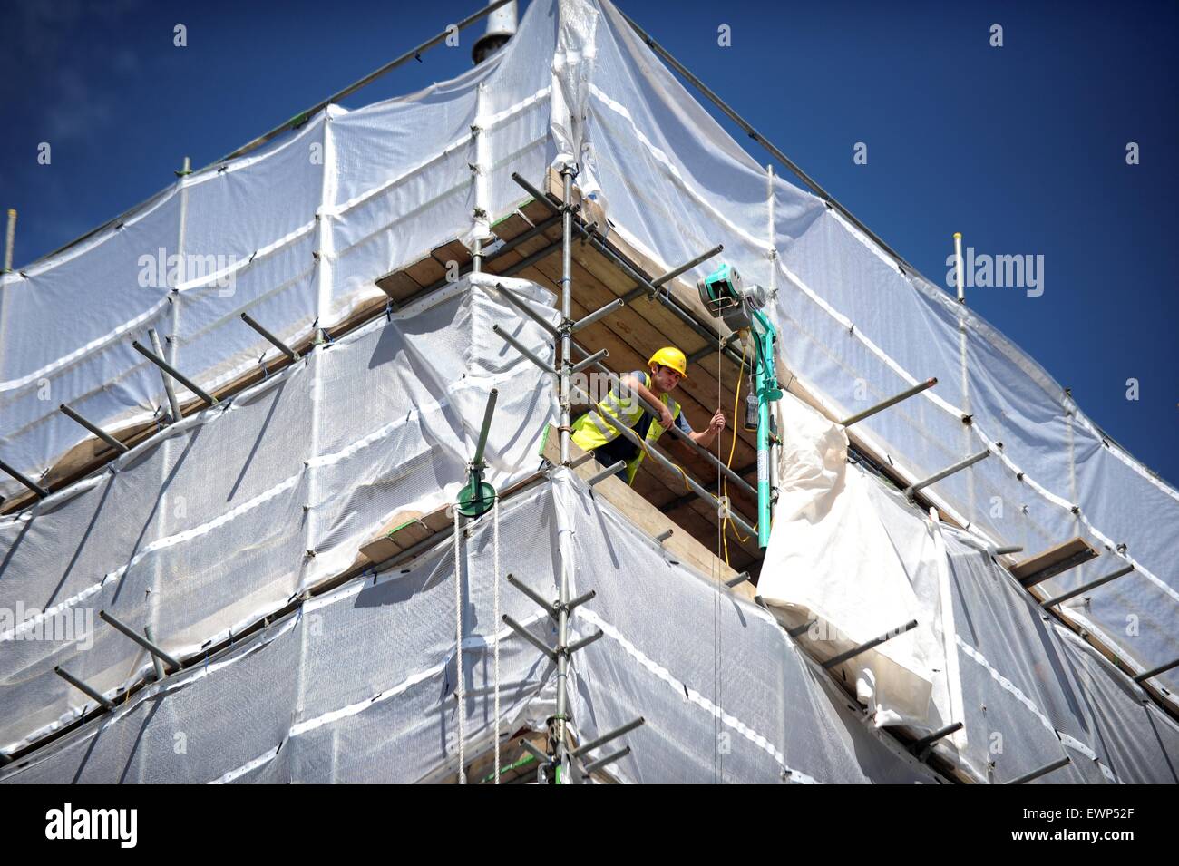 Un trabajador de la construcción se asoma de andamios en un sitio de vivienda de nueva construcción. Foto de stock