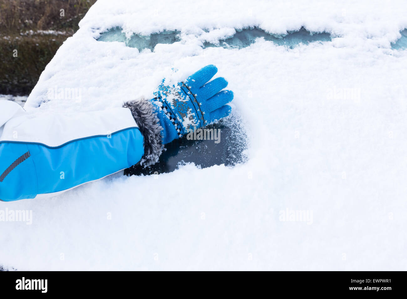 Brazo con guante azul retirar nieve de ventanilla en la temporada de invierno Foto de stock