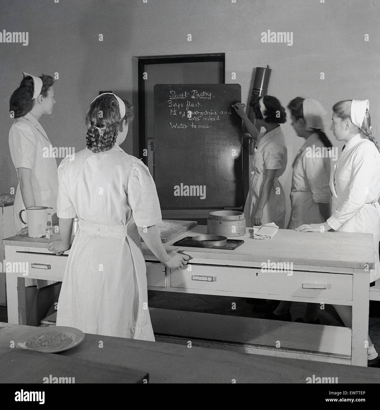 1950, imagen histórica que muestra una clase de cocina, una maestra que escribe en una pizarra una receta vista por un número de estudiantes o aprendices, Inglaterra, Reino Unido. Foto de stock