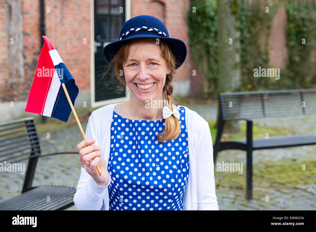 Mujer de mediana edad caucásico vestido con ropa azul celebrando el día de la liberación con la bandera holandesa Foto de stock