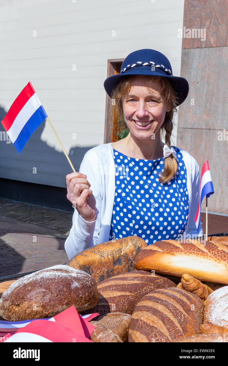 Mujer caucásica con panes saludando con bandera holandesa para celebrar el día de la liberación en Holanda Foto de stock