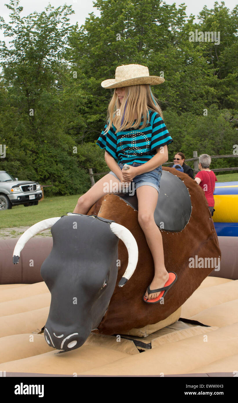 Jóvenes pre-jovencita cabalga un toro mecánico en las celebraciones del Día de Canadá en Cannington, Ontario Foto de stock