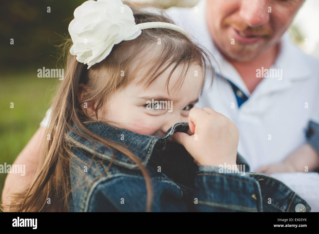 Joven chica sentada con su padre, ocultando el rostro con chaqueta Foto de stock