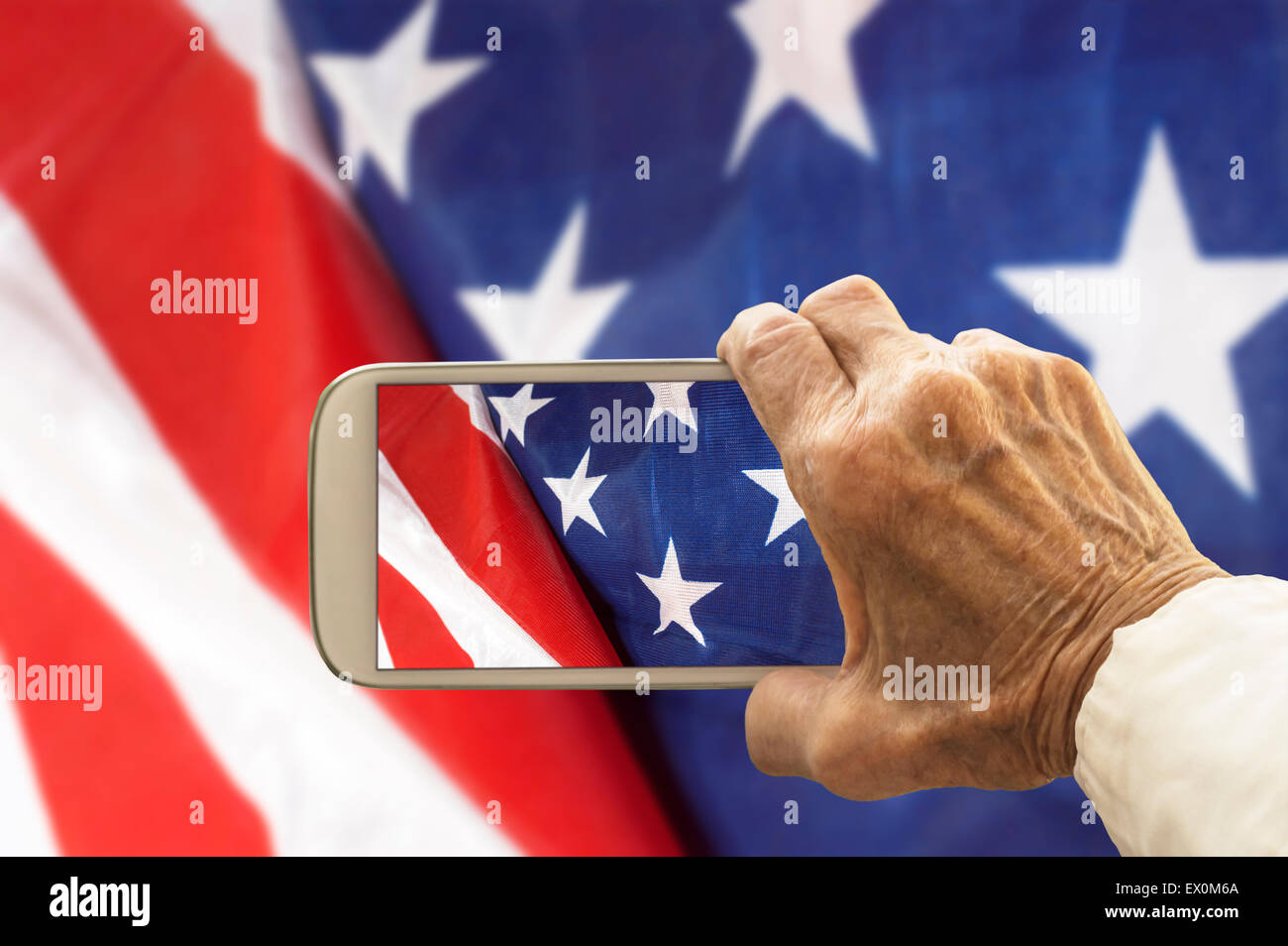 Vieja mano toma una foto de la bandera de Estados Unidos, el teléfono inteligente. Enfoque selectivo Foto de stock