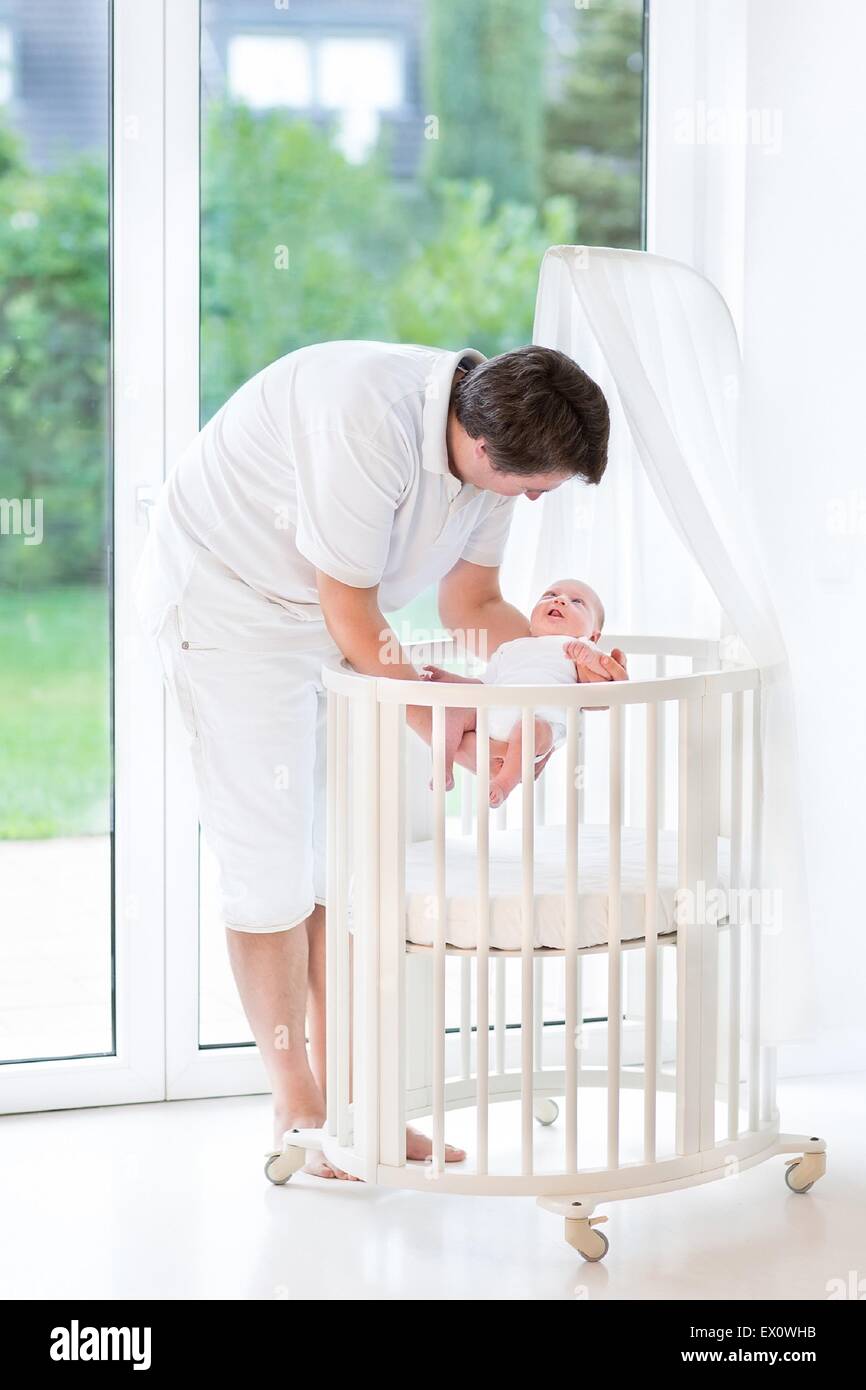 Sonriente joven padre poner a su bebé recién nacido en una cuna redonda  blanca en una gran ventana al jardín Fotografía de stock - Alamy