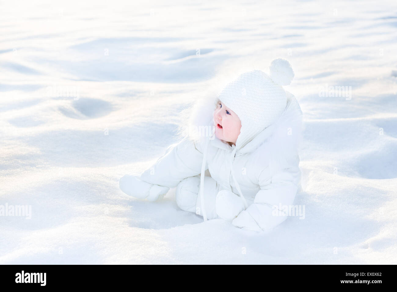 Poco lindo bebé en una chaqueta blanca jugando en la nieve Foto de stock