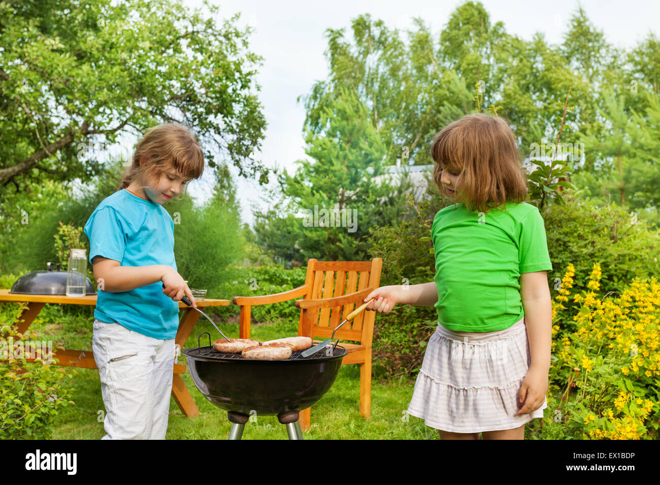 Dos niñas cerca de cocinar carne a la barbacoa en el jardín Foto de stock