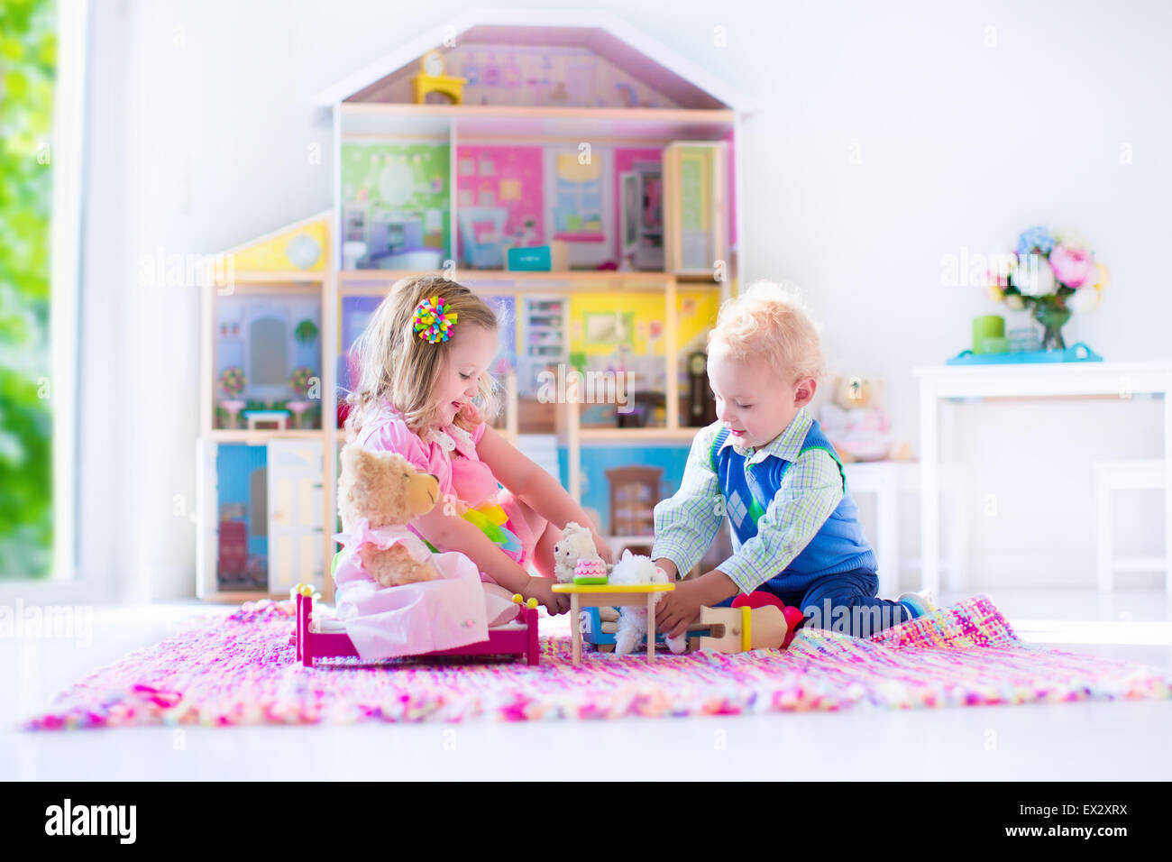 Niños jugando con casa de muñecas y juguetes de peluche. Niños sentados en  una alfombra rosa en una sala de juegos en casa o en el jardín de infantes.  Niño Fotografía de