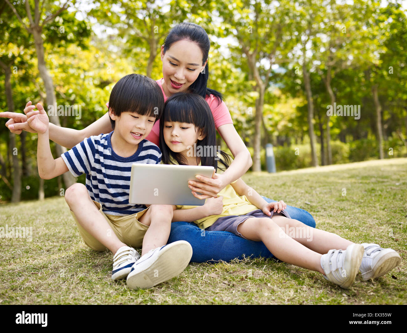 Madre e hijos asiáticos usando el ipad en el exterior. Foto de stock