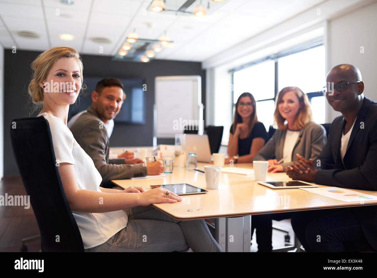Grupo de jóvenes ejecutivos sonriendo a la cámara durante una reunión de trabajo. Foto de stock