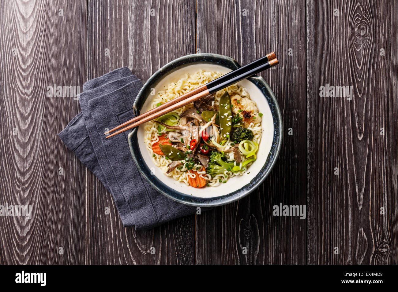 Fideos asiáticos con setas y verduras en un tazón sobre fondo de madera gris Foto de stock
