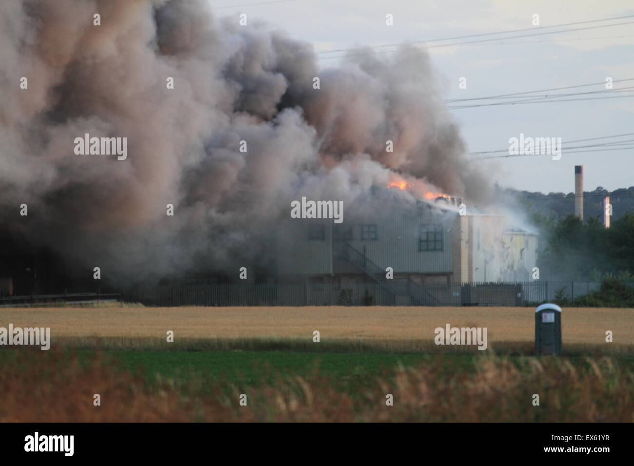 Rainham, Londres, Reino Unido. Martes, 7 de julio de 2015. Más de 80 bomberos abordar blaze en un astillero de palets en Rainham. 12 bomberos de tres bomberos fueron llamados a la escena alrededor de las 8:00pm el martes por la noche. Kent y Essex, bomberos y servicios de rescate fueron llamados para ayudar a afrontar la Brigada de Bomberos de Londres Blaze. Una pila de palets y un número de edificios están implicados en el incendio. Formulario de humo el incendio podría ser visto por millas alrededor de vientos atizado las llamas. No hay informes de lesiones y la causa de la llamarada no se conoce todavía. Foto de stock