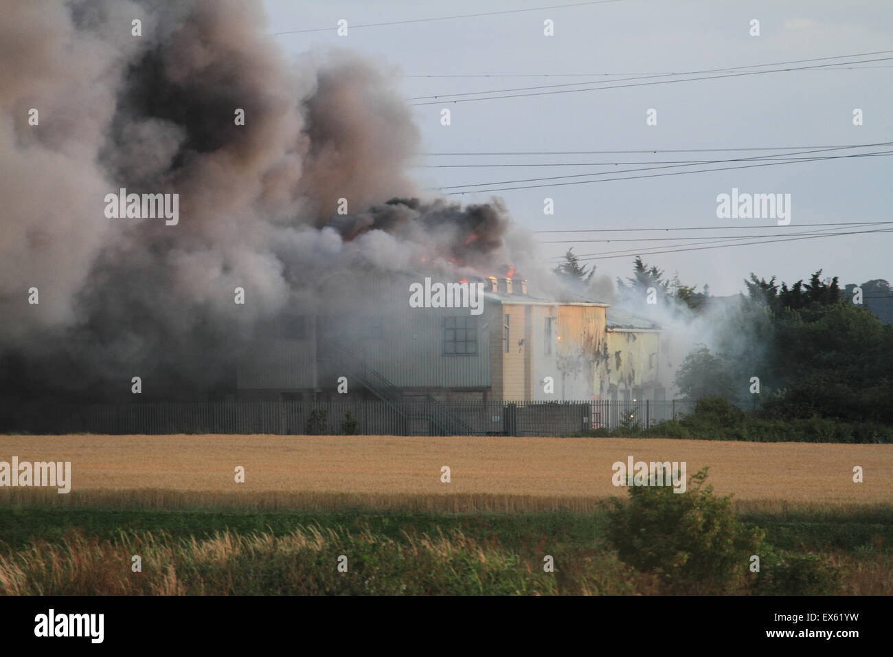 Rainham, Londres, Reino Unido. Martes, 7 de julio de 2015. Más de 80 bomberos abordar blaze en un astillero de palets en Rainham. 12 bomberos de tres bomberos fueron llamados a la escena alrededor de las 8:00pm el martes por la noche. Kent y Essex, bomberos y servicios de rescate fueron llamados para ayudar a afrontar la Brigada de Bomberos de Londres Blaze. Una pila de palets y un número de edificios están implicados en el incendio. Formulario de humo el incendio podría ser visto por millas alrededor de vientos atizado las llamas. No hay informes de lesiones y la causa de la llamarada no se conoce todavía. Foto de stock