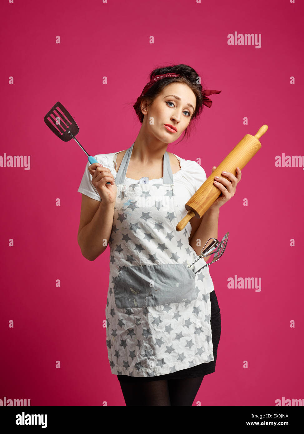Gracioso ama de casa y utensilios de cocina, fondo de color rosa Foto de stock