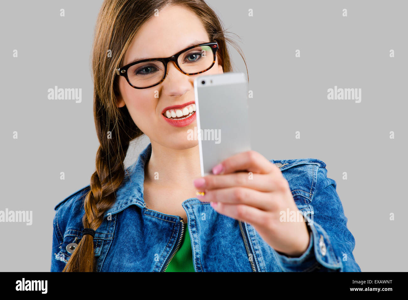 Bella mujer tomando un selfie y haciendo un rostro feo, aislado sobre un fondo gris Foto de stock