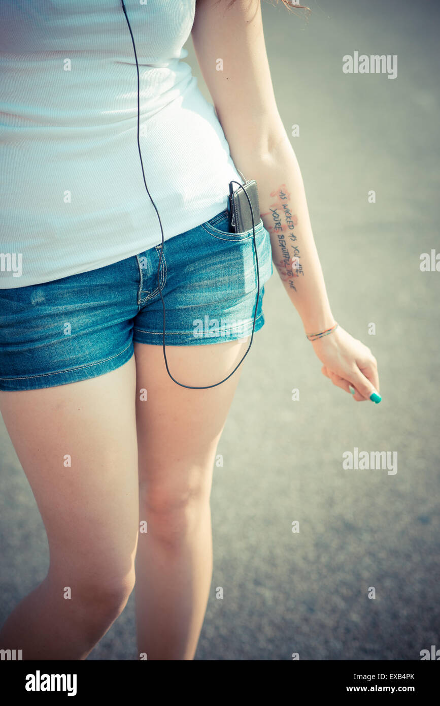 Cerca de la hermosa joven de largo cabello rizado hipster mujer piernas escuchando música con el smartphone en la ciudad Foto de stock
