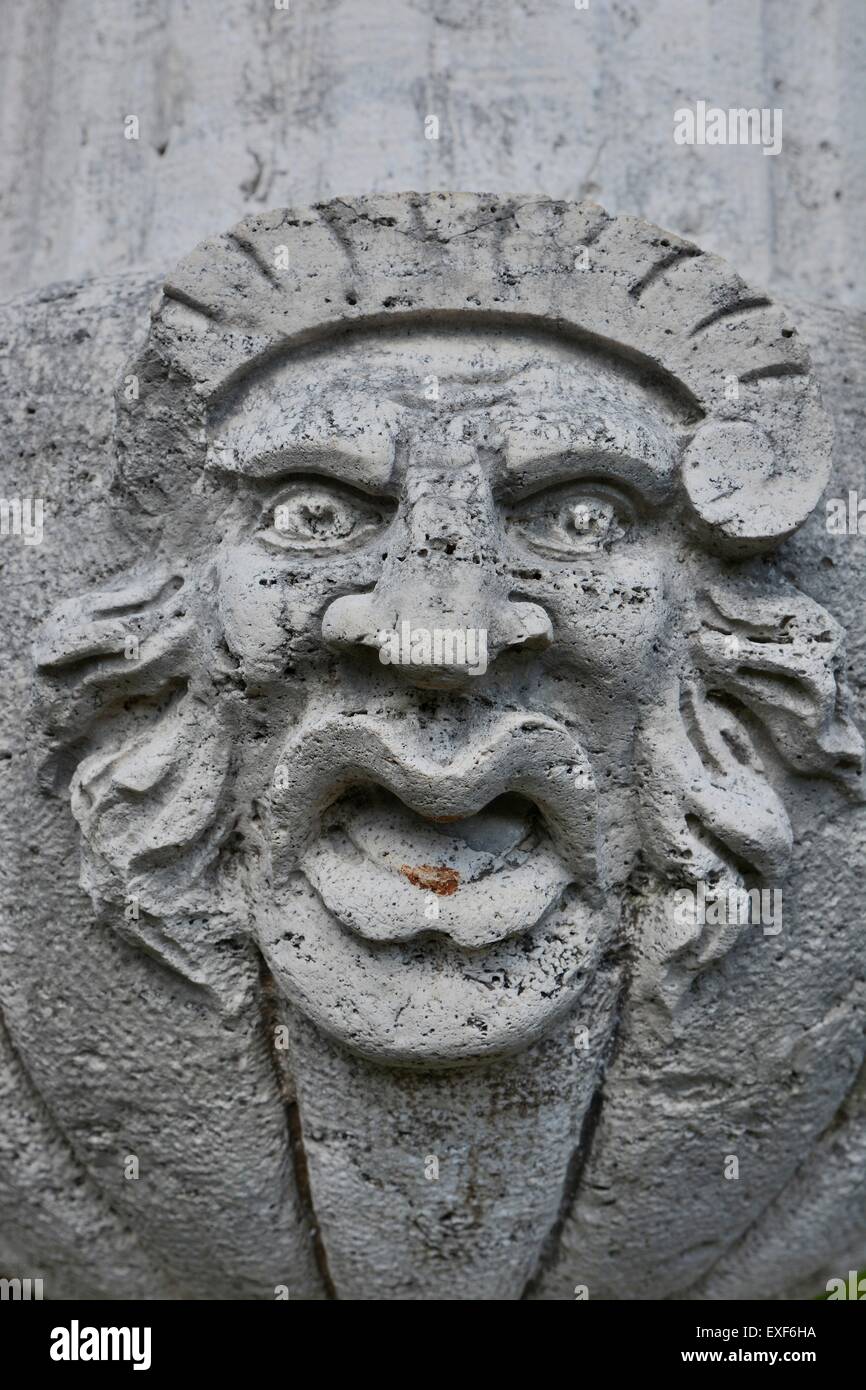 Escultura fea cara en muro de piedra Foto de stock