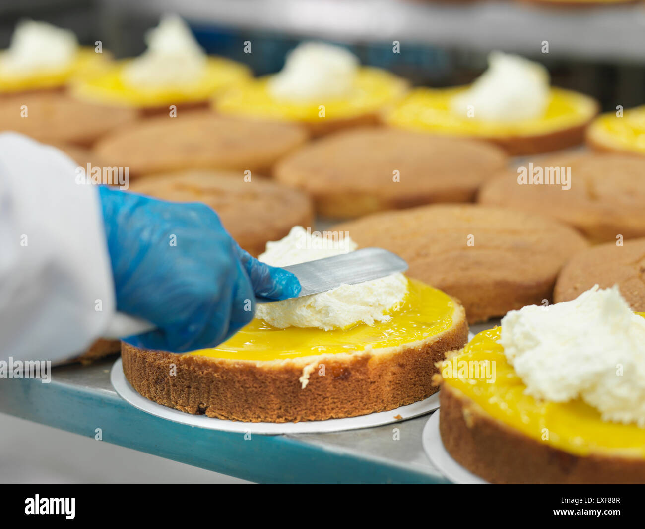 Trabajadora propagación de relleno en tartas en fábrica de pastel, cerrar Foto de stock