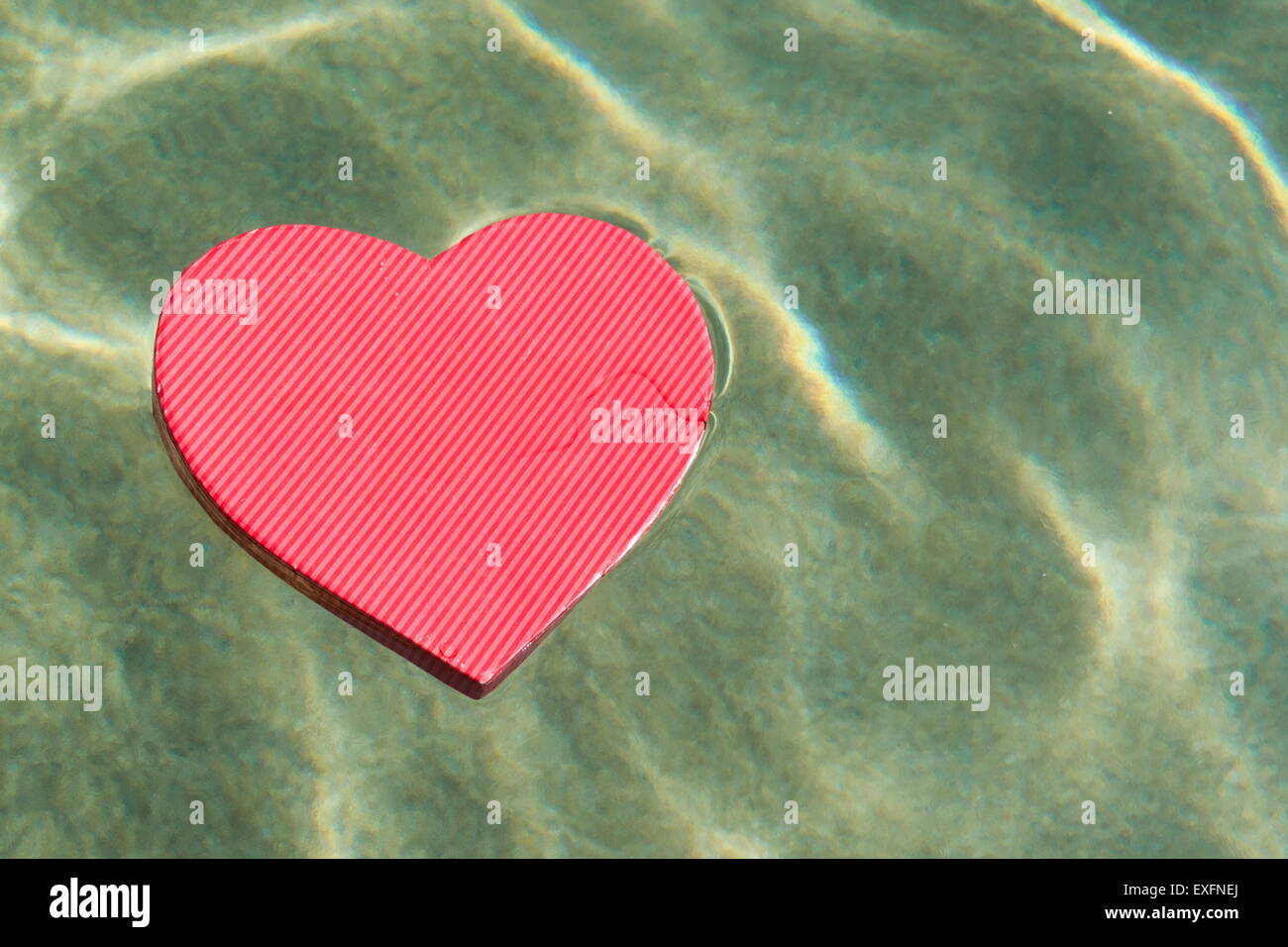 Presente en forma de corazón rojo caja flotando en la superficie del mar Foto de stock