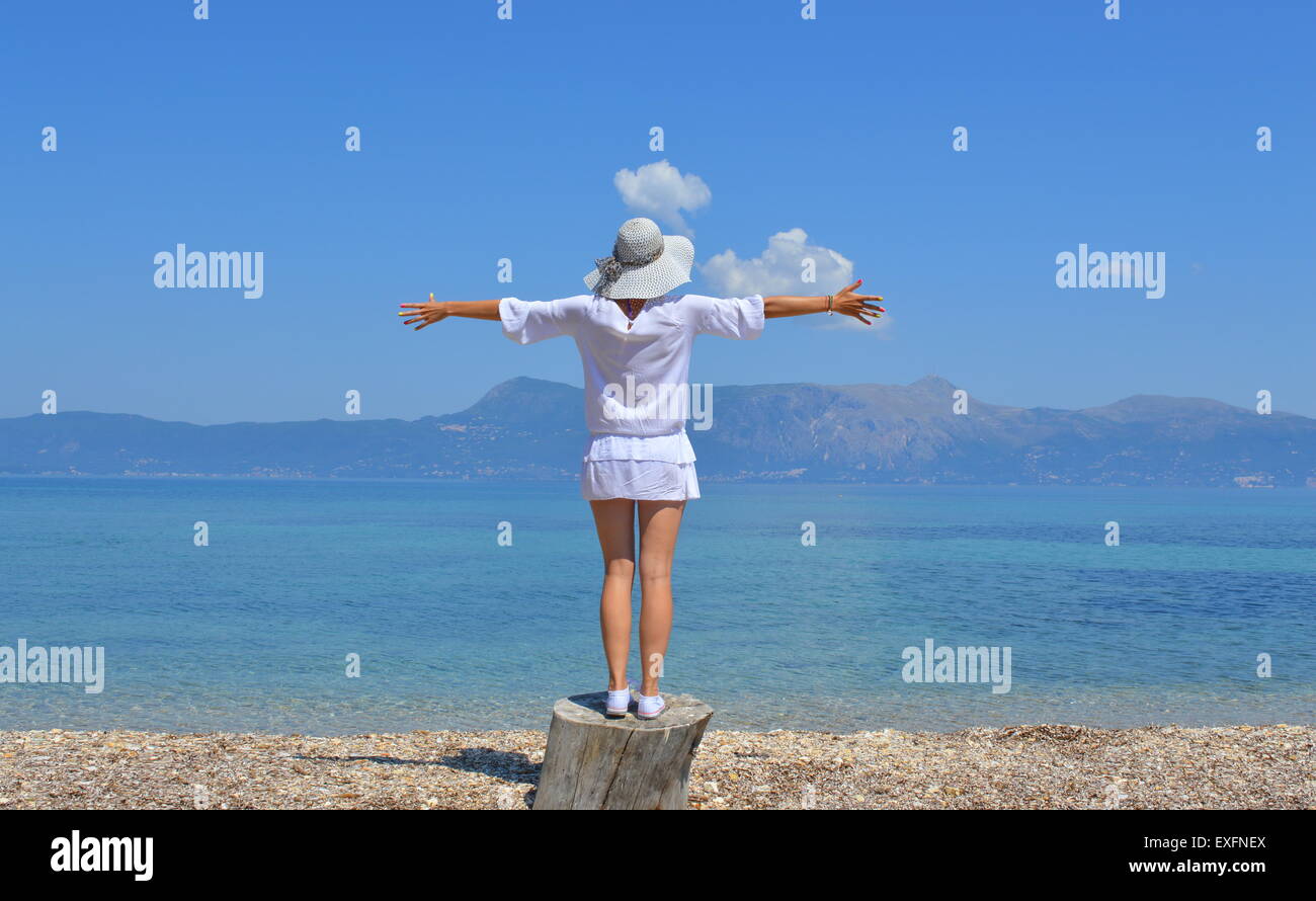 Mujer joven mirando las montañas sobre el mar con sus brazos abiertos en un día soleado de verano Foto de stock