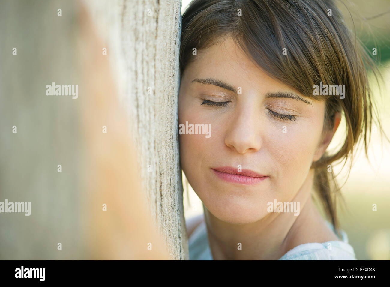 Mujer RECOSTADA contra el tronco del árbol con los ojos cerrados, Retrato Foto de stock