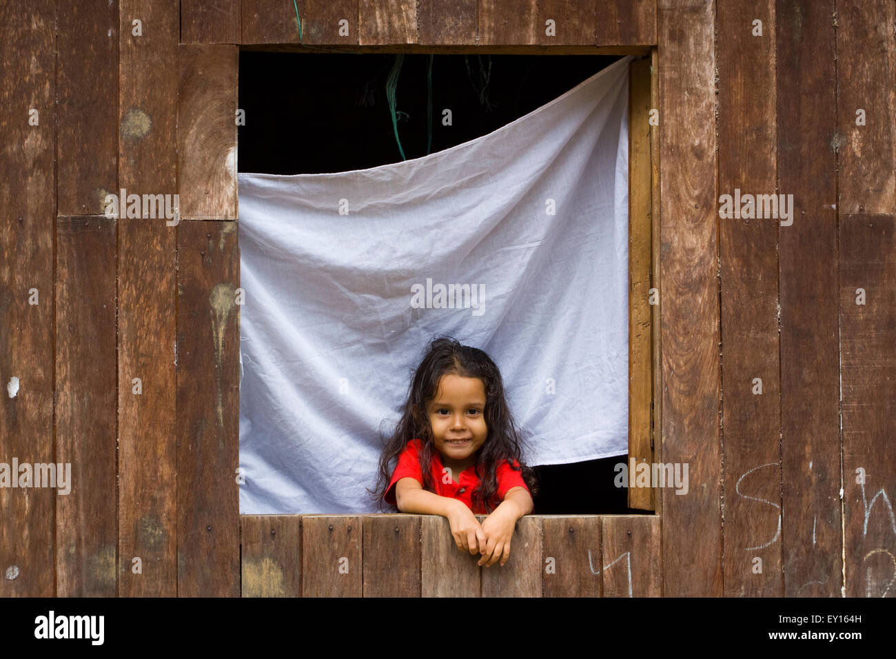 Cute Little Girl en la ventana de su casa de madera sonriendo ante la cámara en el Castillo, Nicaragua Foto de stock