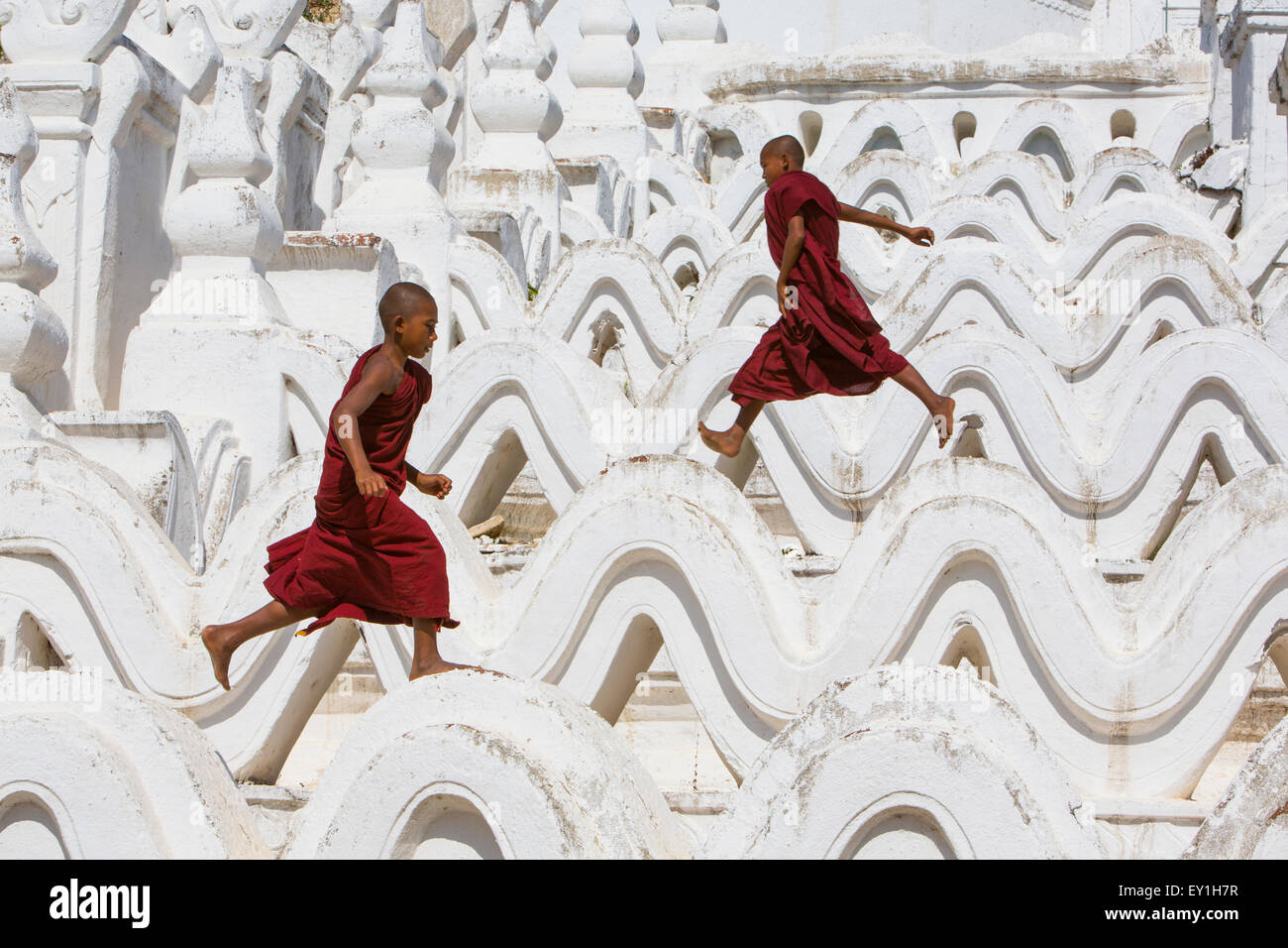 Los monjes novicios túnicas rojas saltando olas en Hsinbyume Paya templo, Mandalay, Myanmar Foto de stock