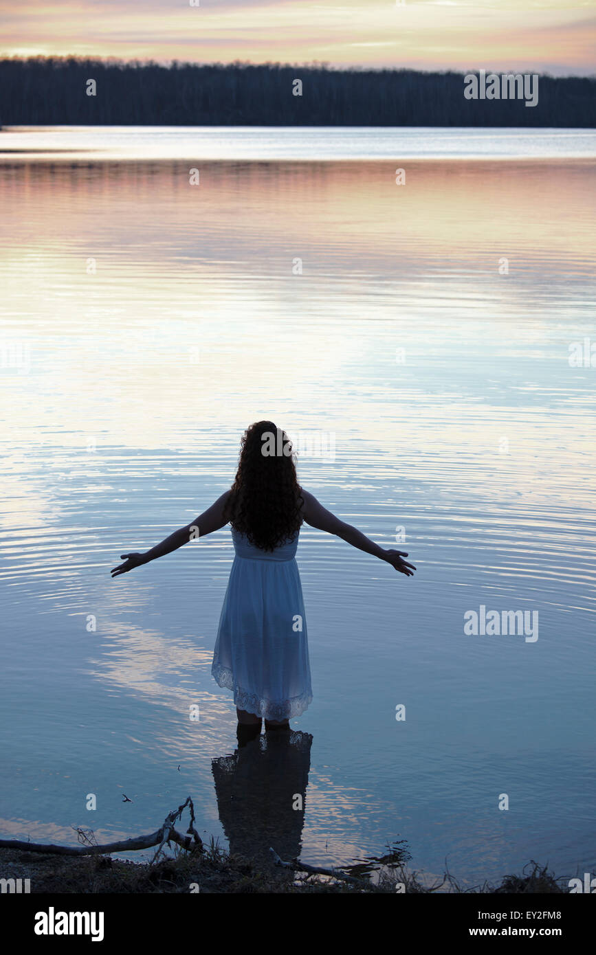 Una mujer en un vestido blanco en aguas poco profundas en el crepúsculo Foto de stock