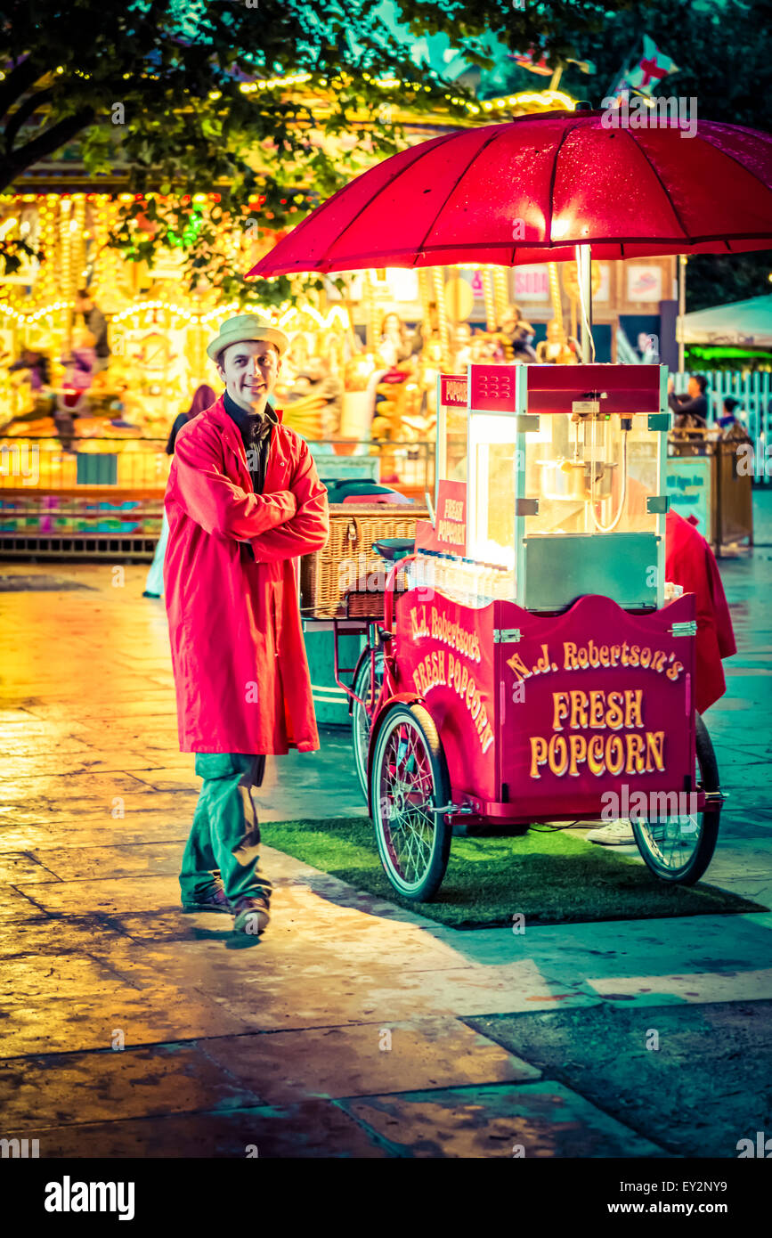 Un vendedor de palomitas de maíz con su puesto en frente de una feria tradicional carrusel de noche Foto de stock