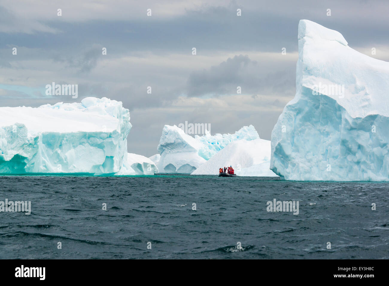 Grupo de personas cruzando el océano en la Antártida en un bote de goma, icebergs en el fondo. Foto de stock