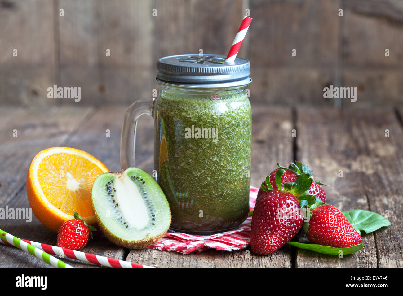 Saludable batido verde de espinacas, kiwi, fresas y naranjas en una jarra  con paja roja sobre una tabla de madera Fotografía de stock - Alamy