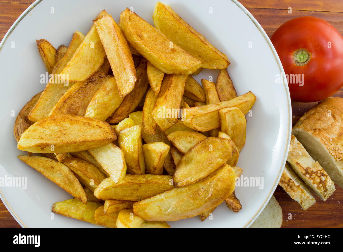 Patatas fritas caseras en una placa decorada con rodajas de pan y un tomate Foto de stock