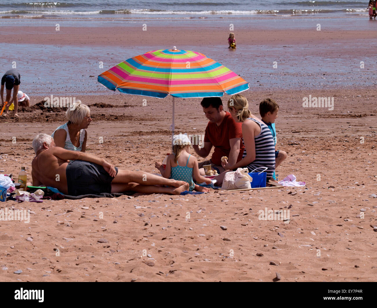 Tres generaciones de la misma familia haciendo un picnic junto a la playa, Goodrington Sands Paignton, Devon, Reino Unido Foto de stock