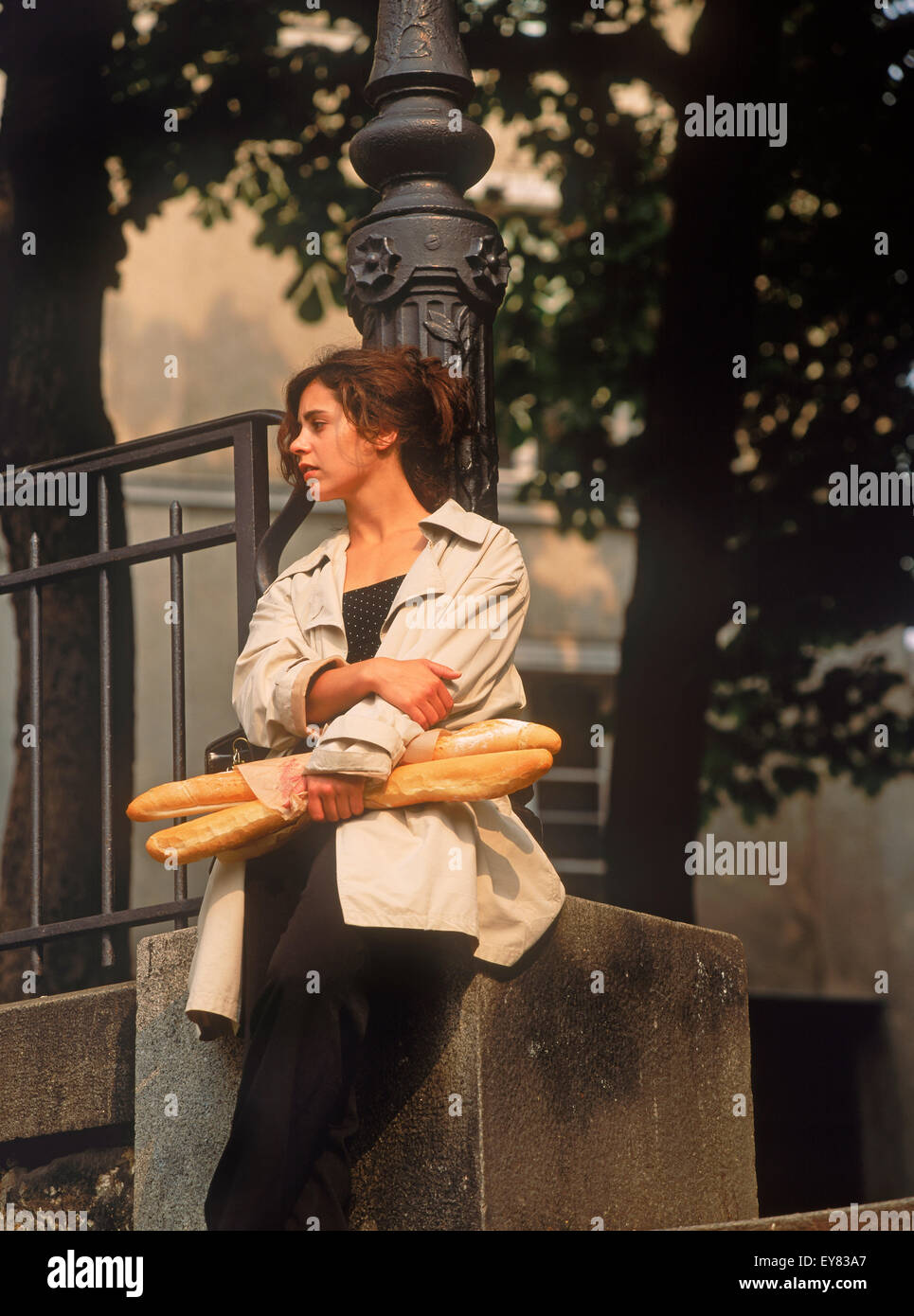 Mujer parisina con baguettes apoyado contra la lámpara de la calle post en la tranquila plaza de Montmartre Foto de stock