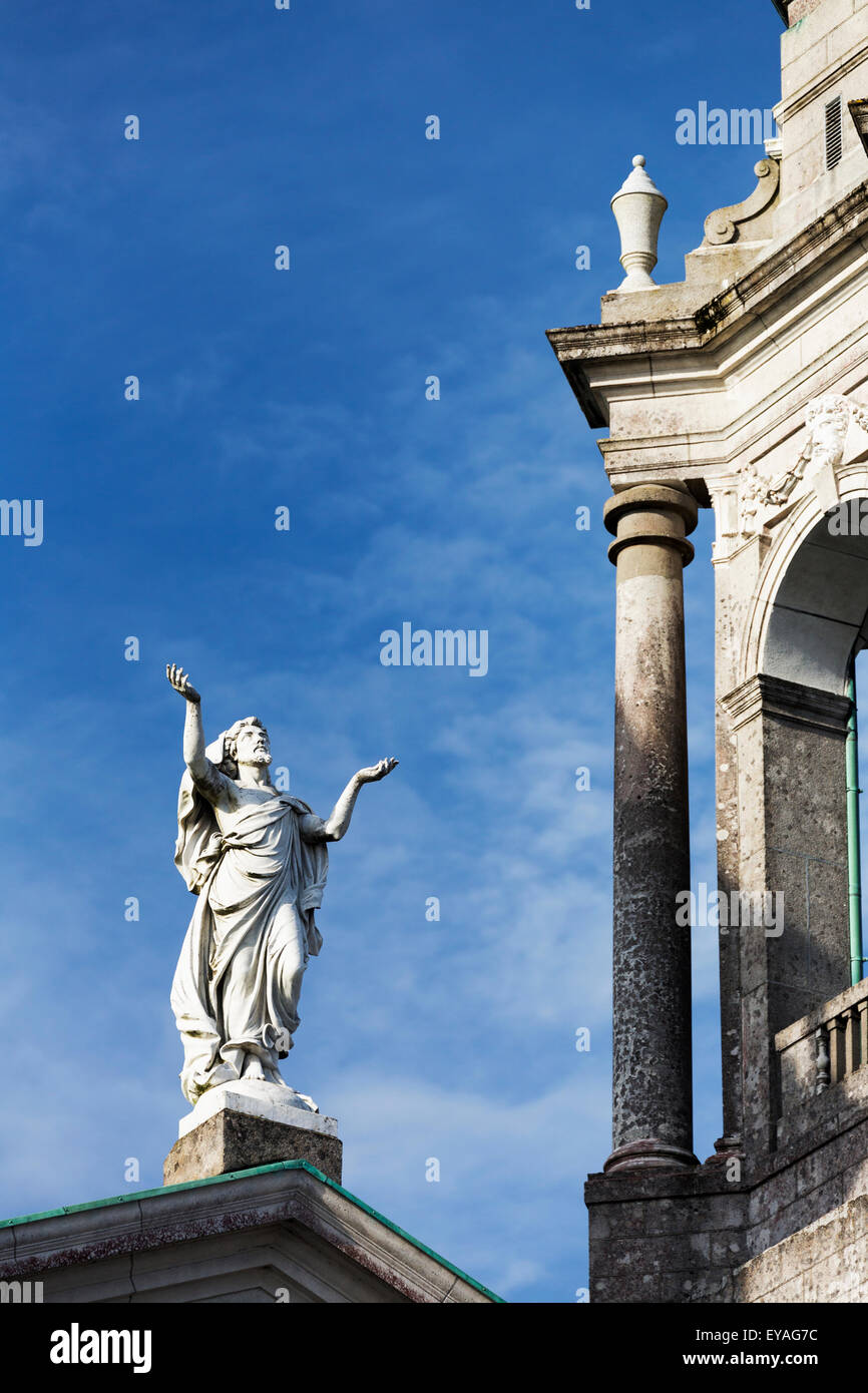 Estatua de hombre barbado elevando los brazos hacia el cielo con el campanario de la iglesia y el cielo azul; Athlone, Condado de Westmeath, Irlanda Foto de stock
