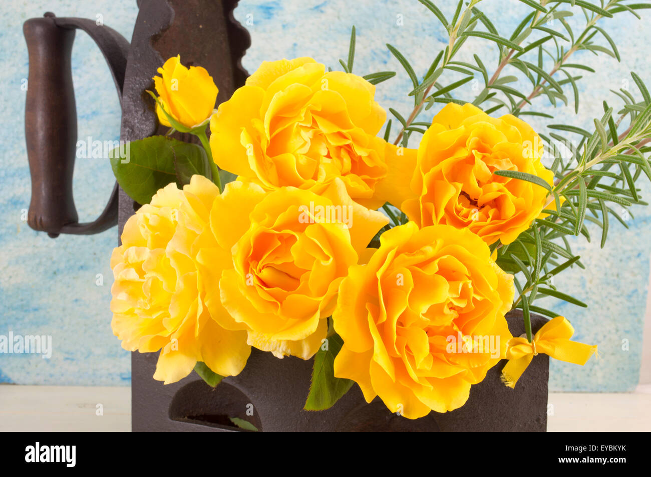 Bouquet de rosas amarillas con romero en una vendimia de hierro como florero, sobre una mesa de madera Foto de stock